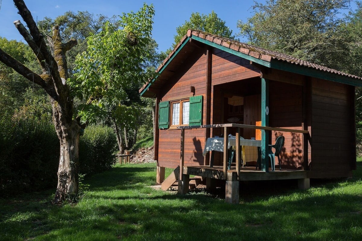 A wooden cabin with a porch, surrounded by trees and grass.