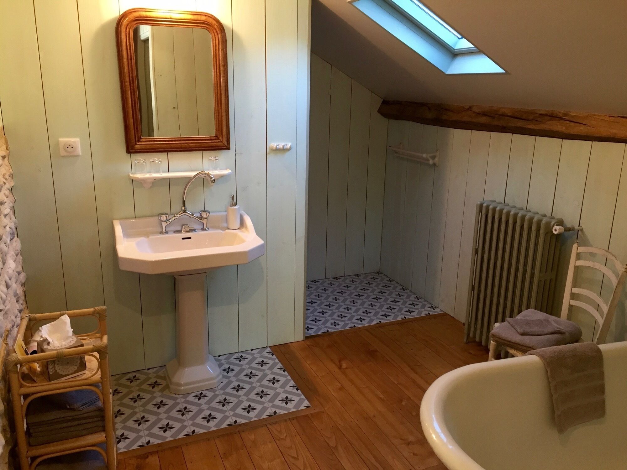 A bathroom with a wooden floor, a white sink, a mirror, a radiator, and a skylight.