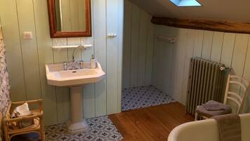 A bathroom with a wooden floor, a white sink, a mirror, a radiator, and a skylight.