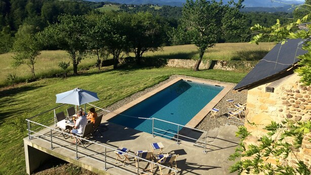 Piscina com vista para montanhas, cercada por árvores e um edifício de pedra.