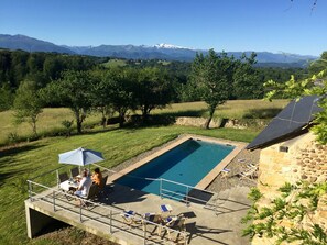Una piscina con vistas a montañas, rodeada de árboles y un edificio de piedra.