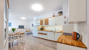 A modern kitchen with white cabinets, a wooden countertop, and a kettle. - Apartamenty Sun & Snow Na Solnej (Kolobrzeg)