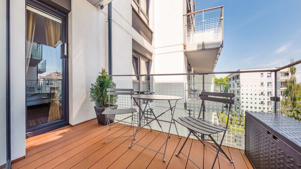 A balcony with a wooden floor, a small table, two chairs, and a potted plant. - Apartamenty Sun & Snow Na Solnej (Kolobrzeg)