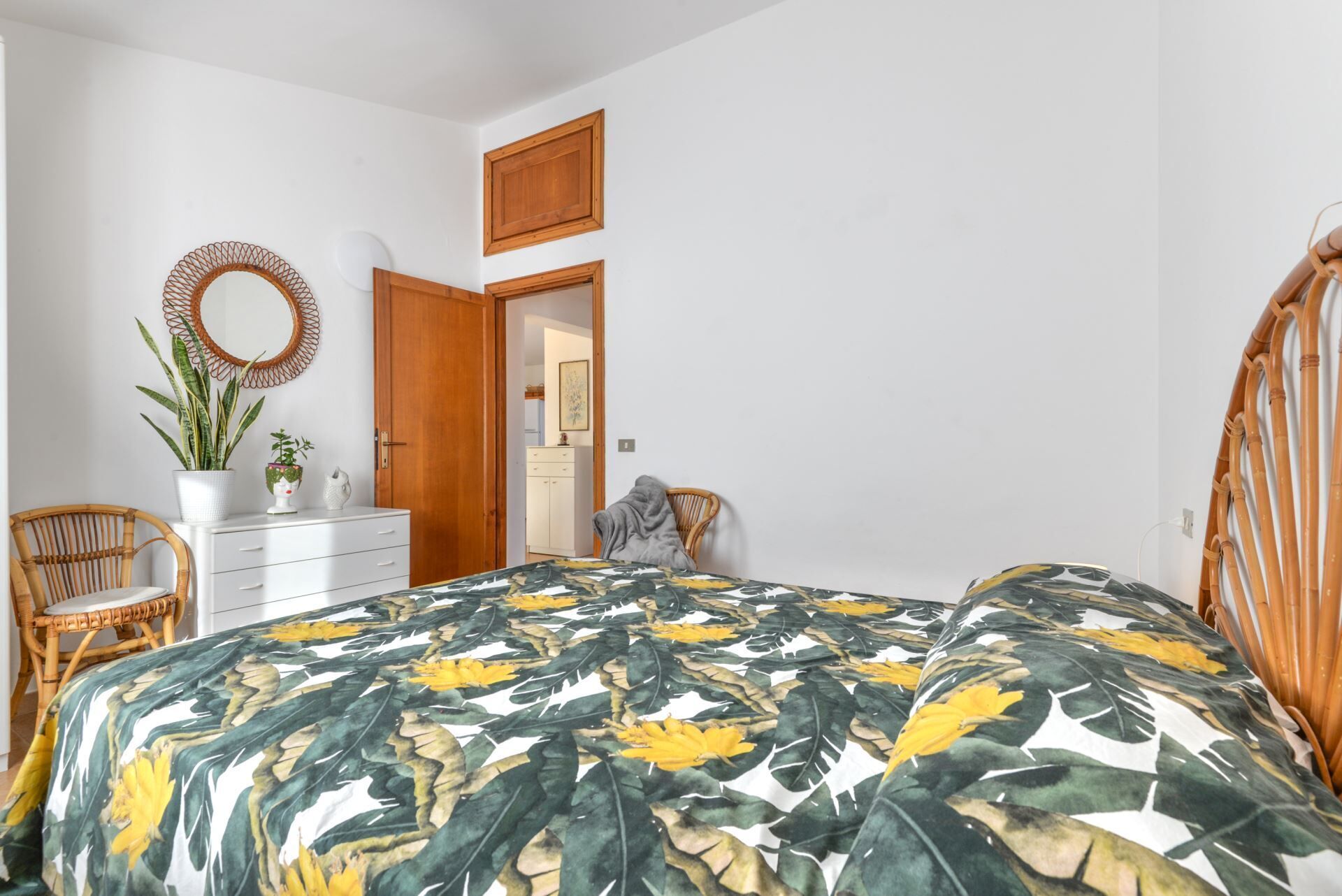 A bedroom with a bed, a dresser, a mirror, and a door leading to another room.