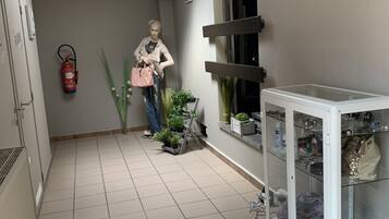 A hallway with a tiled floor, a fire extinguisher, a potted plant, a white cabinet with glass doors, and a framed picture on the wall.