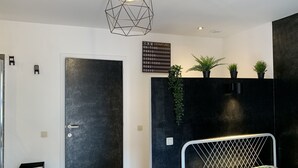 A modern bedroom with a geometric light fixture, a black door, and a sign listing departure destinations. - Carpe Diem (Charleroi)