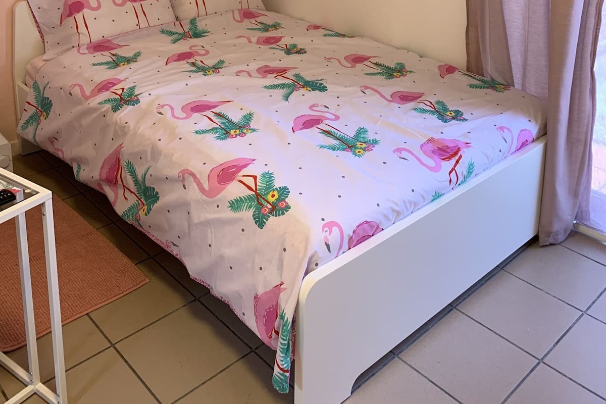 A bedroom with a bed, a TV mounted on the wall, and a window with curtains.