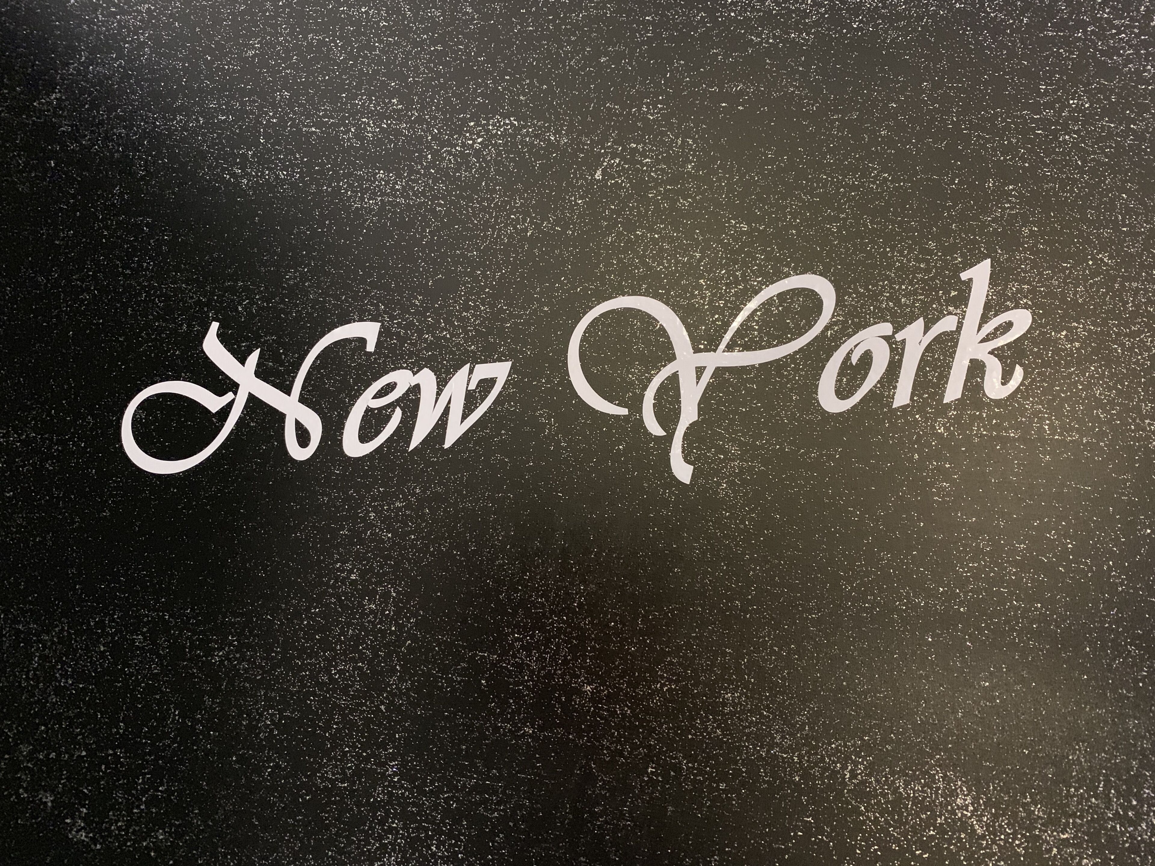 Der Schriftzug „New York“ in kursiver Schrift auf einer strukturierten Oberfläche.