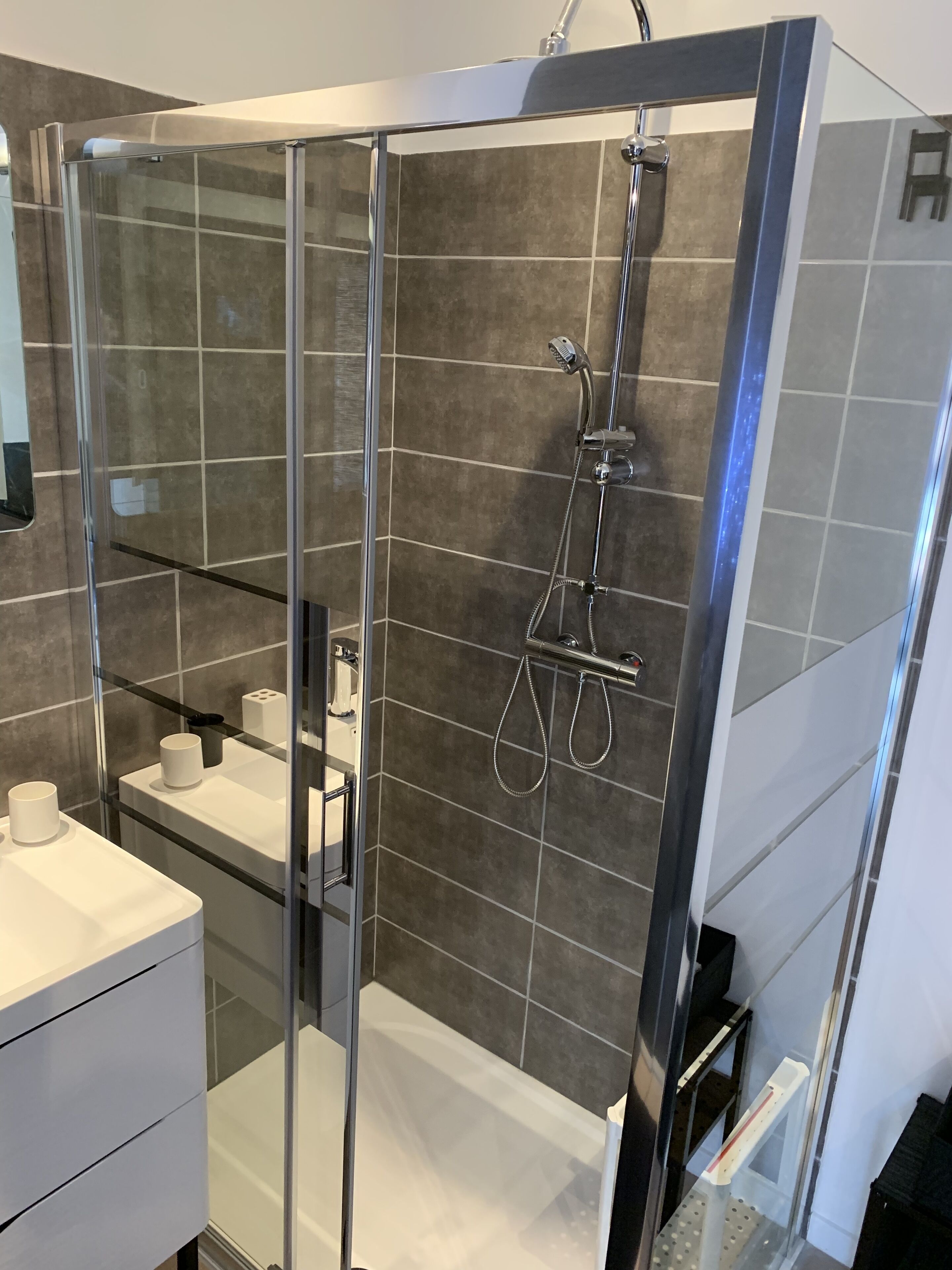 Un baño moderno con ducha de vidrio, lavamanos blanco y un perchero para toallas.