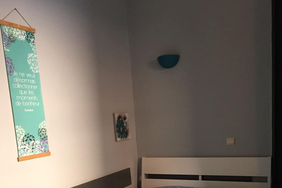 A single bed with a patterned blue bedspread, a wall-mounted decorative item, and a small wall-mounted bowl.