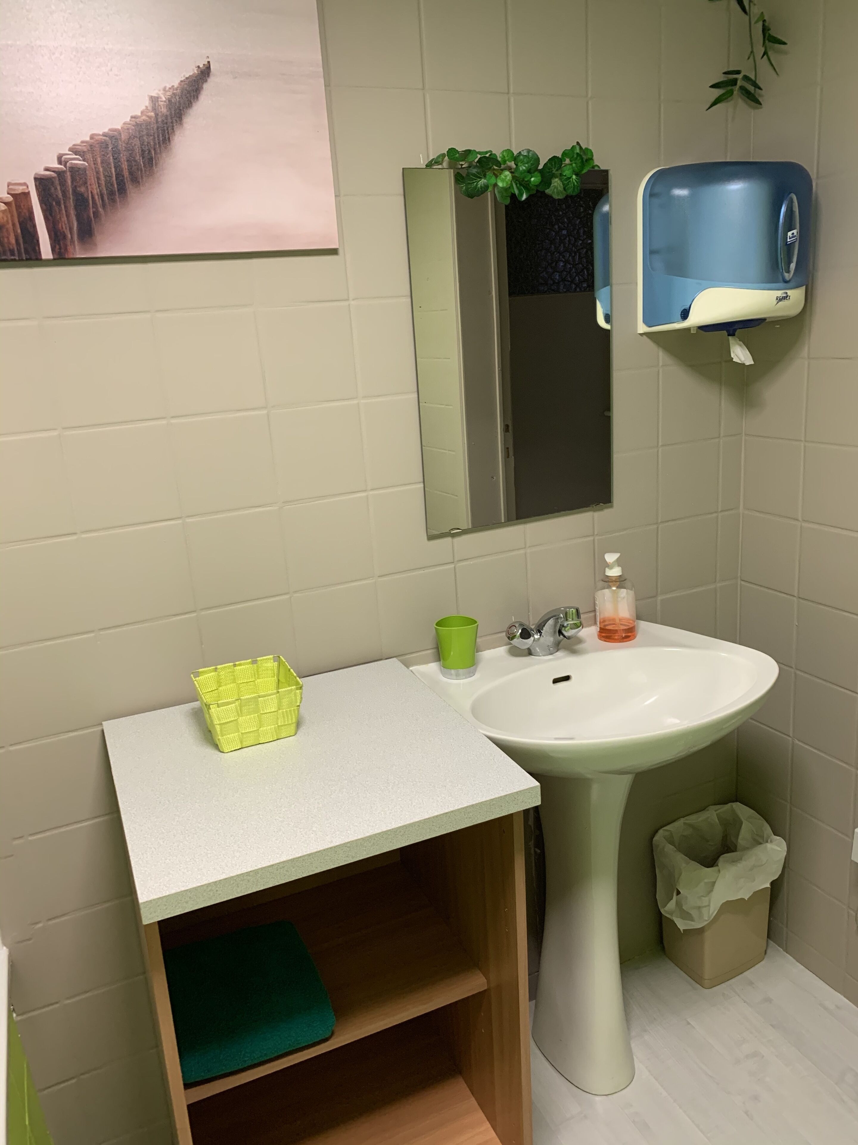 Une salle de bain avec un lavabo blanc, une tasse verte et un panier jaune posés sur le comptoir.