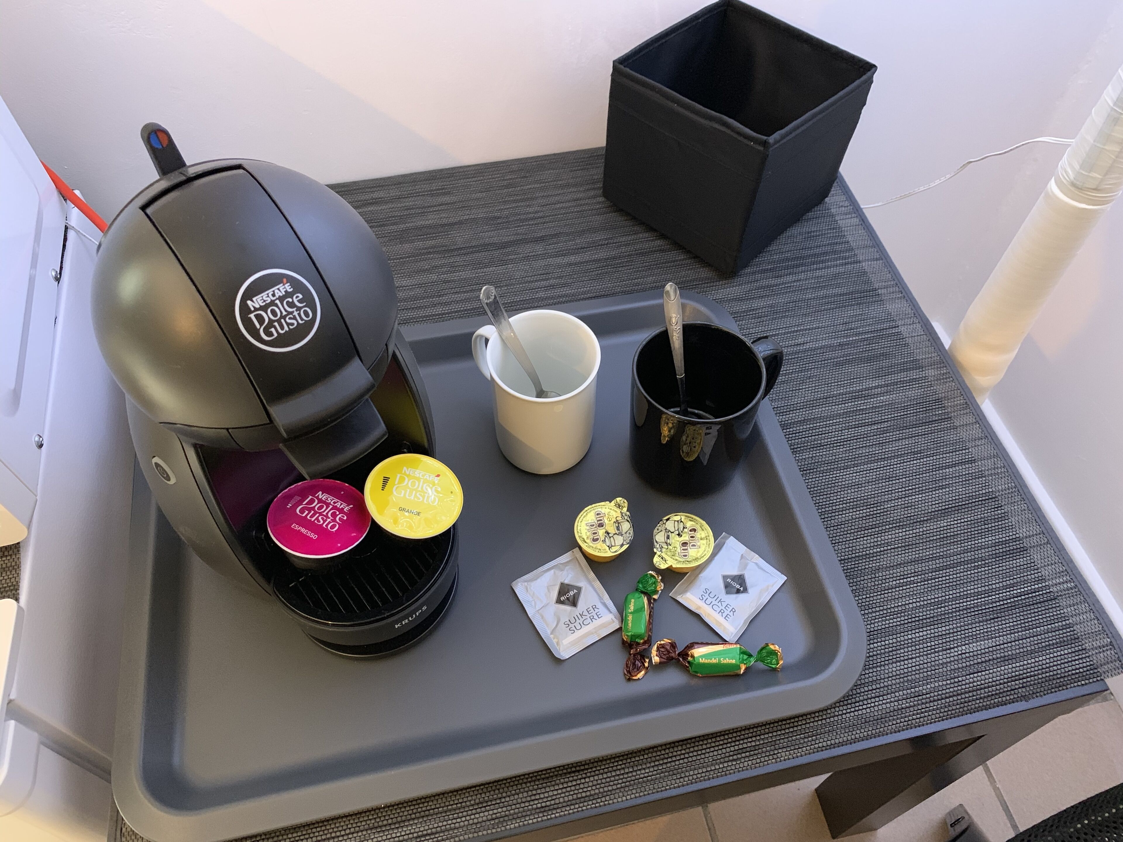 A coffee machine with a tray containing a mug, a cup, a spoon, and some snacks.