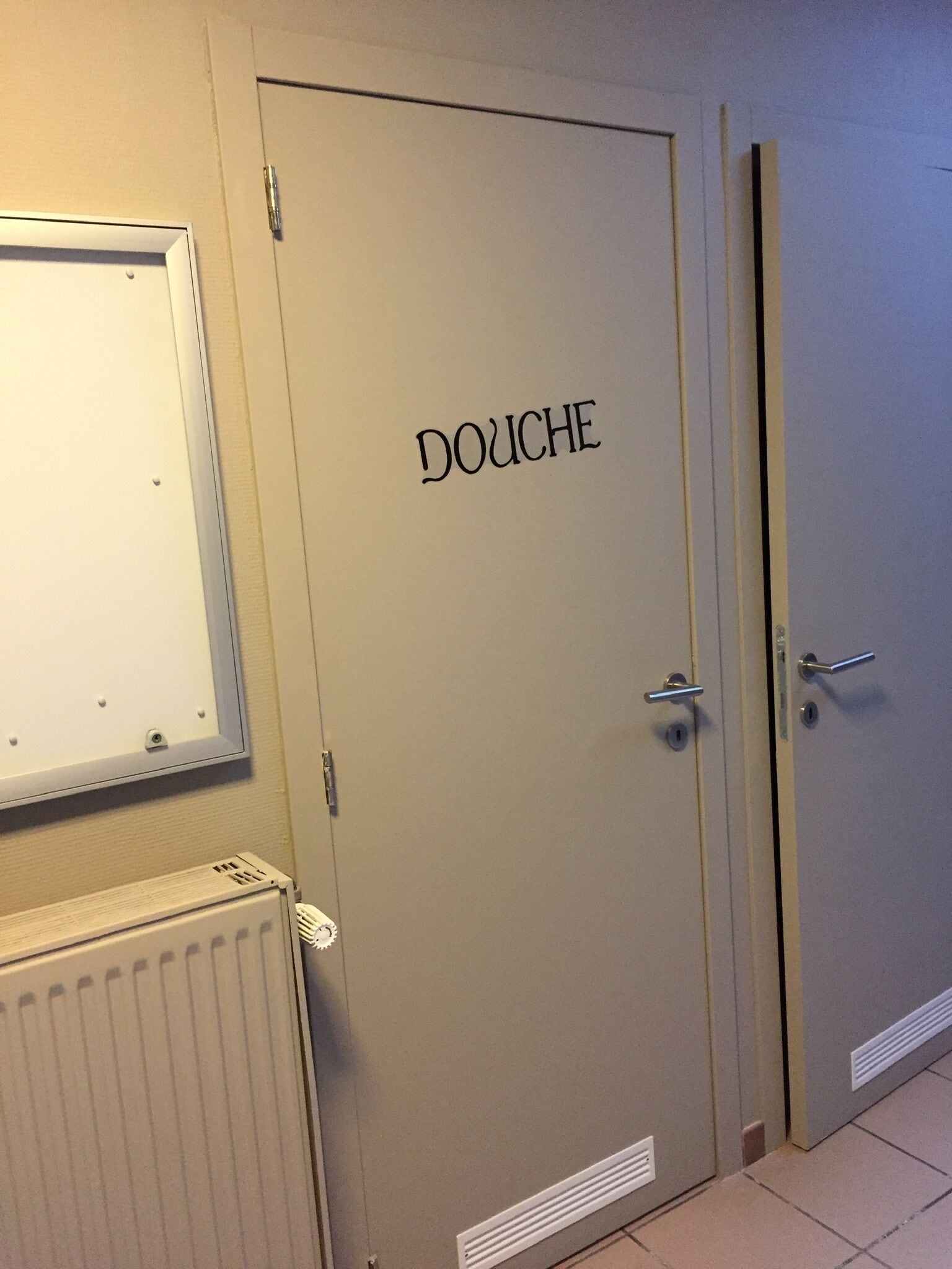 Een deur met de tekst 'DOUCHE', met erboven een radiator en een lamp.