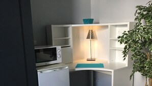 A compact kitchenette with a microwave, a small fridge, and a shelf unit. - Carpe Diem (Charleroi)