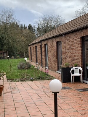 Ein Backsteinhaus mit einer gefliesten Terrasse, einem kleinen Garten und einem weißen Plastikstuhl.