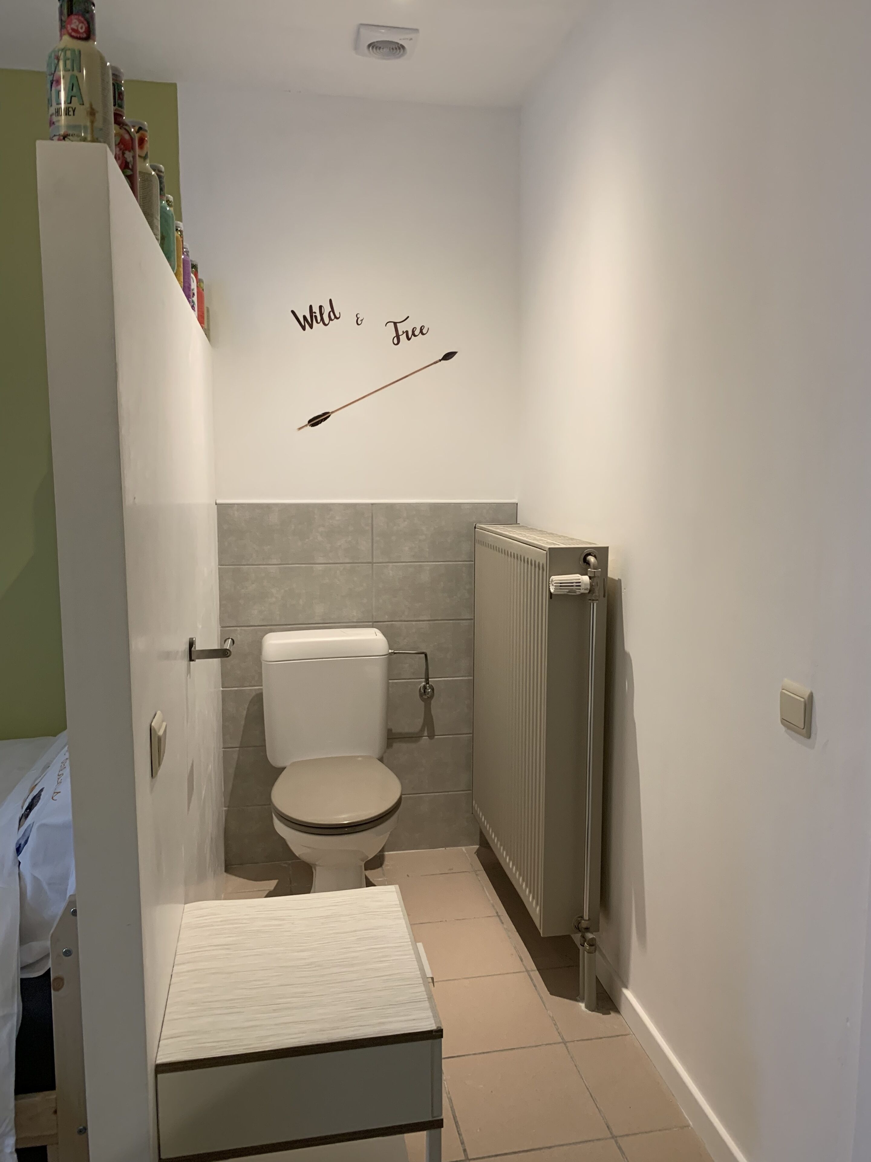 Un baño pequeño con inodoro, un radiador y un estante con artículos de aseo.