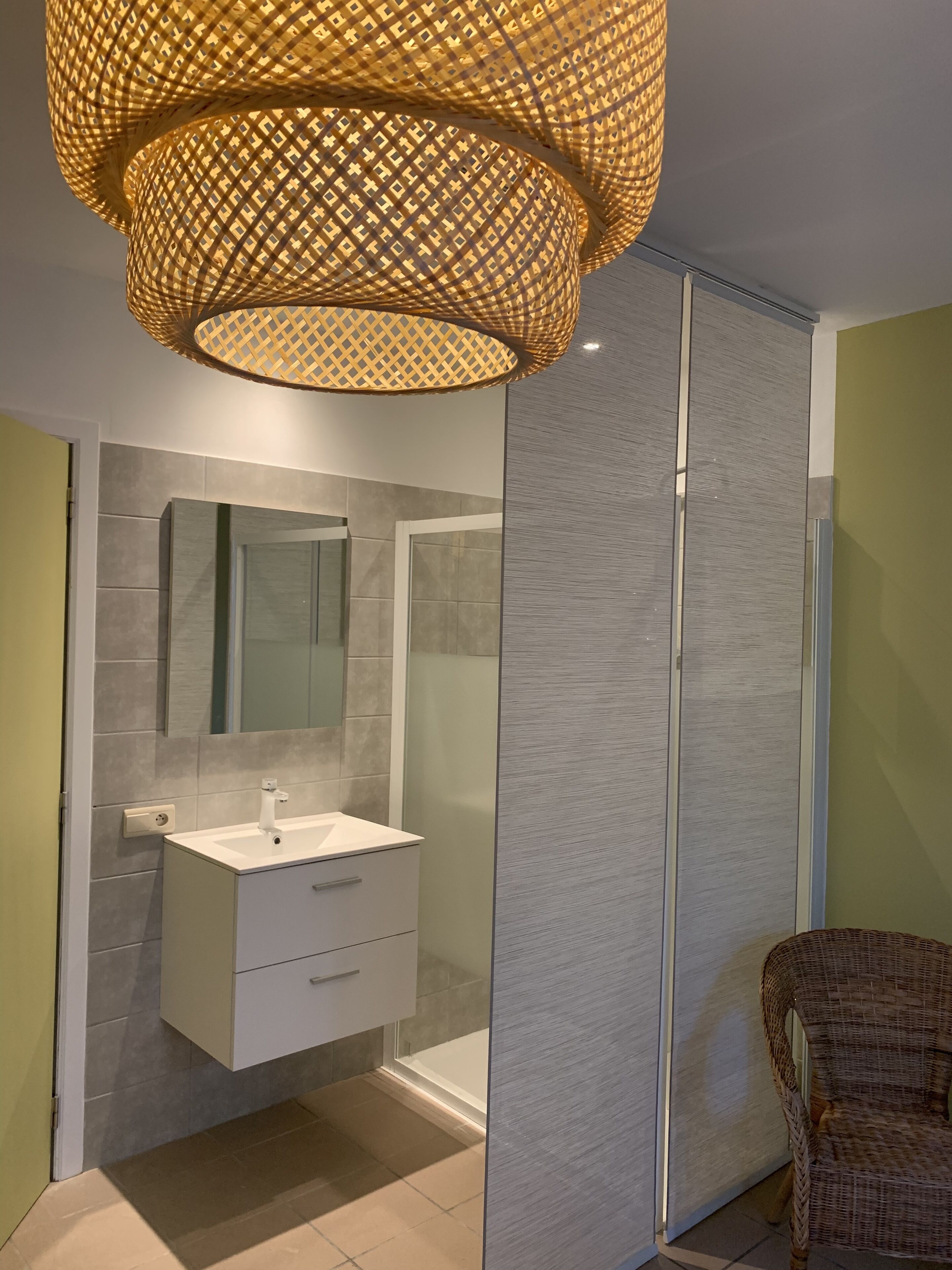 A modern bathroom with a large mirror, white vanity, and a wicker chair.