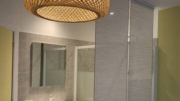 A modern bathroom with a large mirror, white vanity, and a wicker chair.