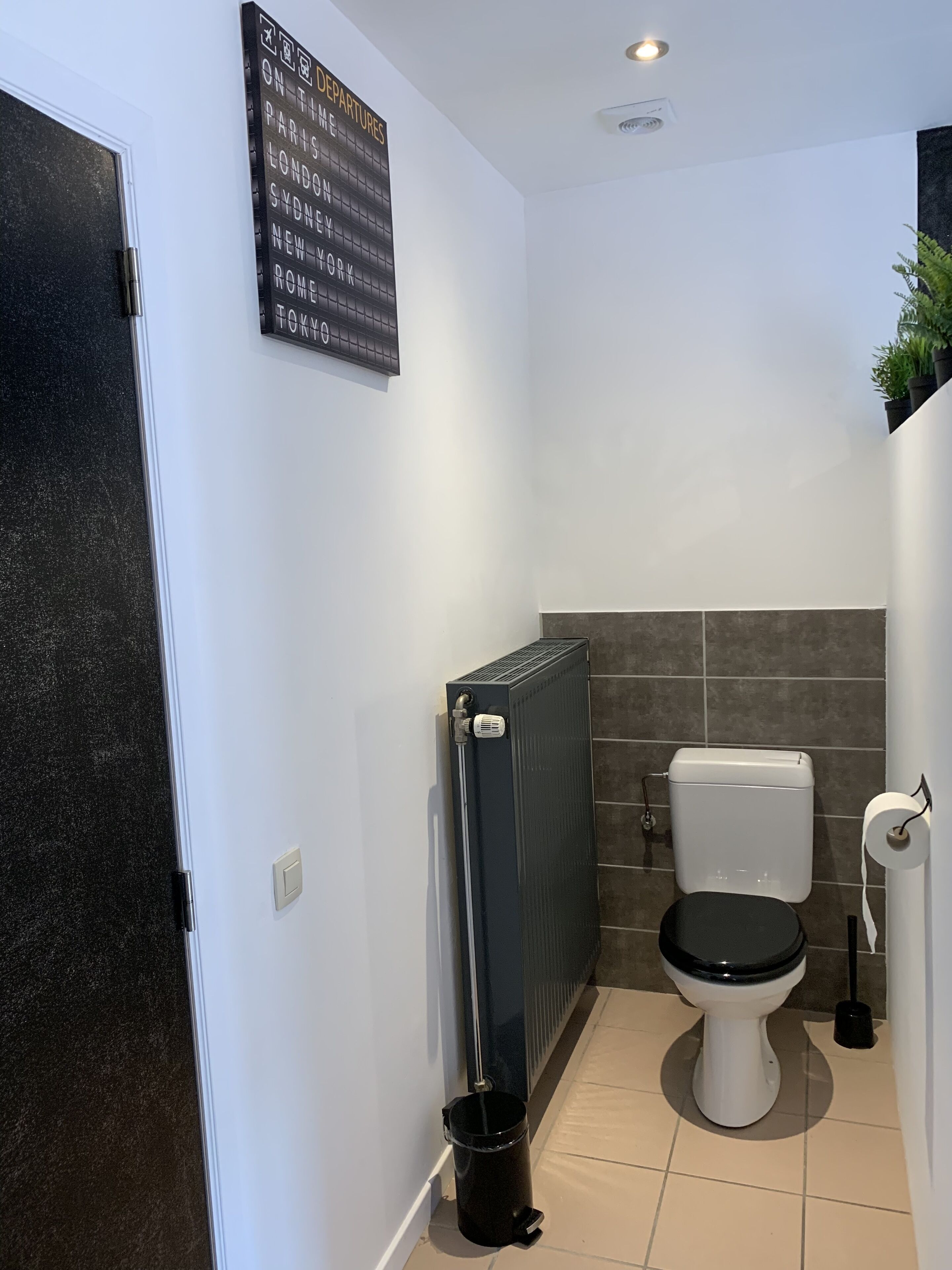 Un baño pequeño con inodoro, radiador y un bote de basura negro.