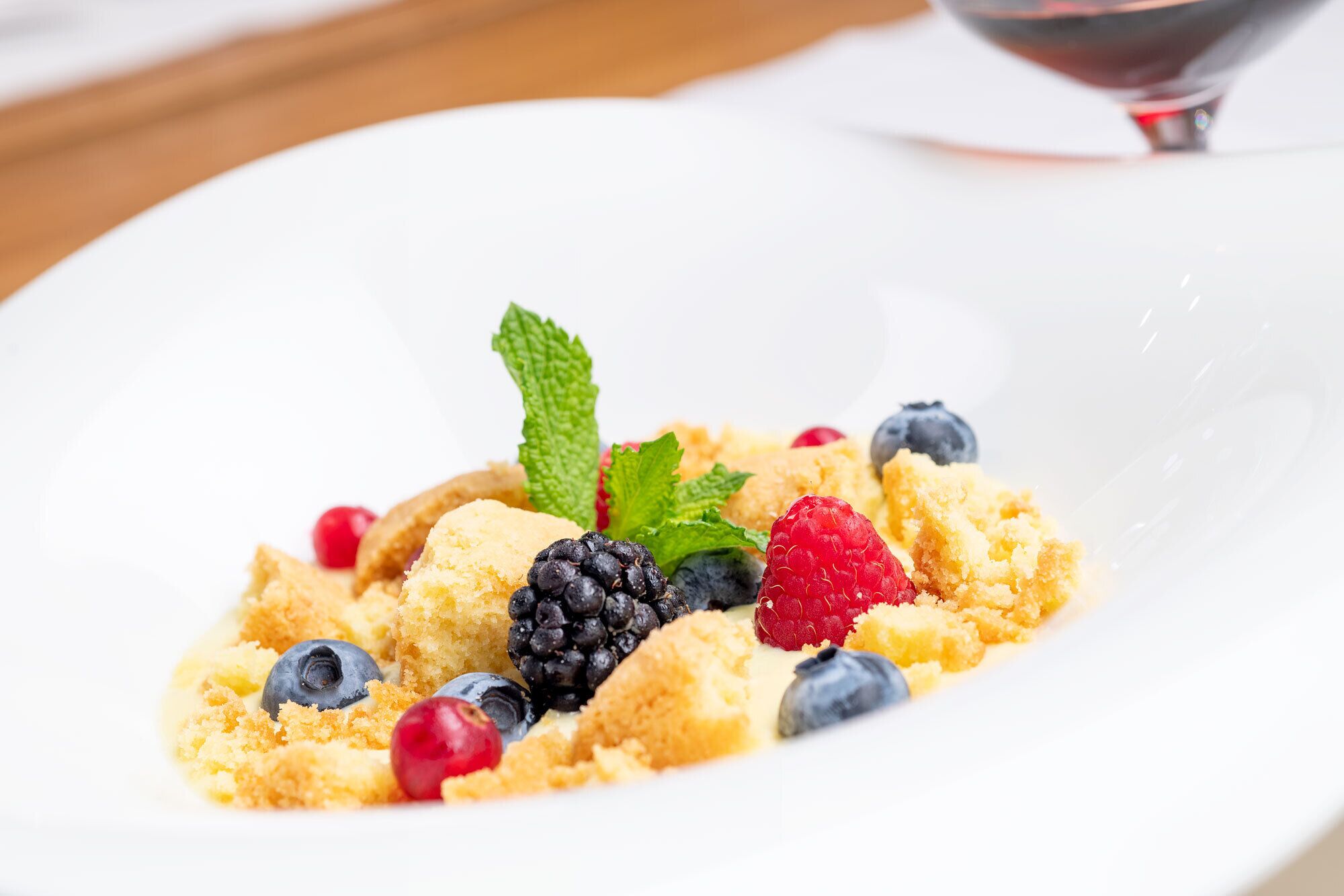 Un plato de postre con fruta y una copa de vino tinto.