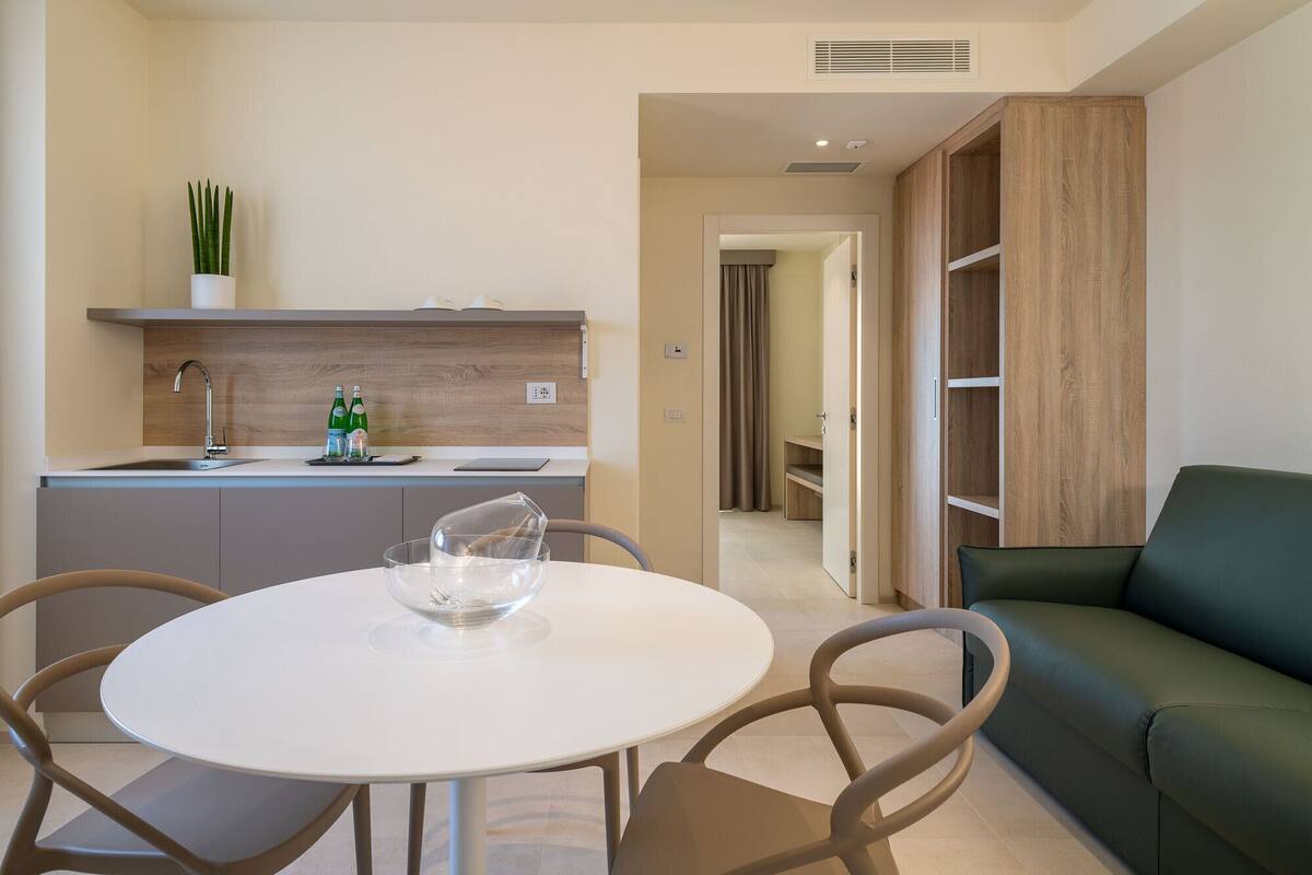A modern kitchen with a white countertop, a built-in sink, and a wooden cabinet. There is a dining area with a white table and chairs.