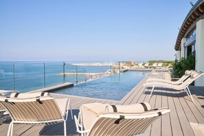 Área da piscina com espreguiçadeiras e vista para o mar.