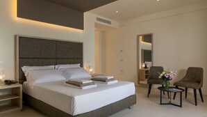Habitación de hotel moderna con una cama grande, mesitas de noche, una pequeña mesa con un florero y una silla.