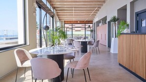 Un comedor moderno con mesas y sillas redondas, ventanas amplias y plantas de interior.