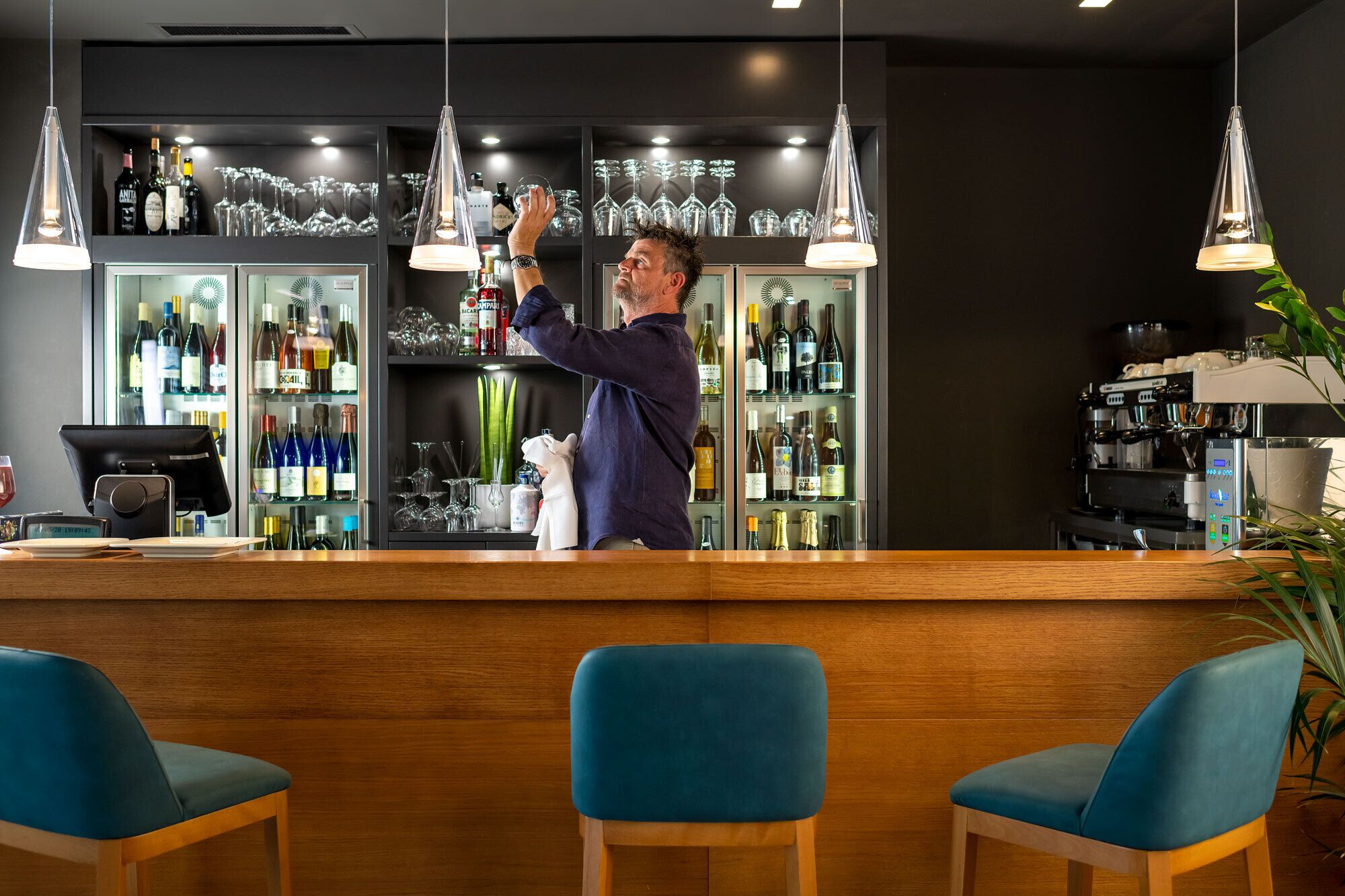A bar area with a bartender, shelves of liquor bottles, glasses, and a coffee machine.