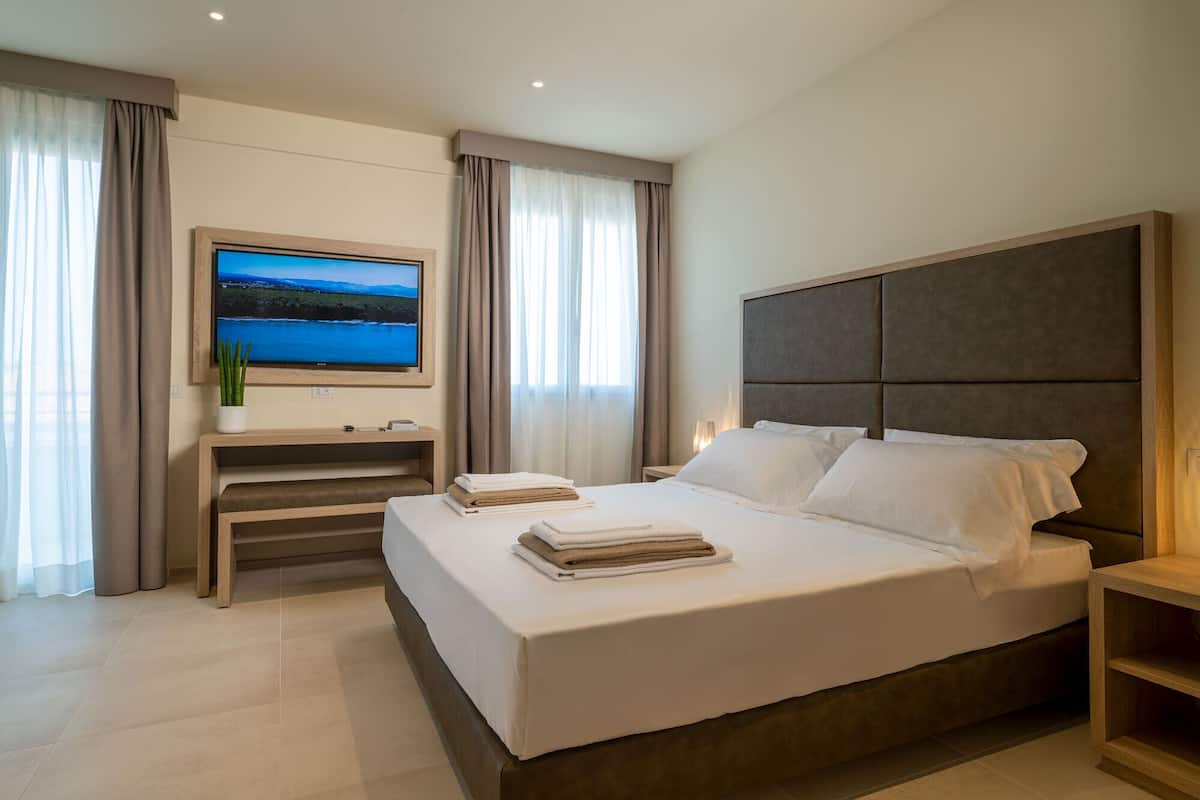 A modern hotel room with a large bed, a flat-screen TV mounted on the wall, a bedside table, and a nightstand.
