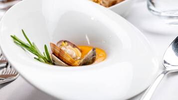 A white plate with clams and a garnish, a spoon, and a glass of water on a table.