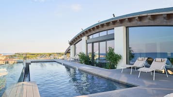 Une piscine à débordement située sur le toit, avec des chaises longues et une vue sur le paysage urbain.