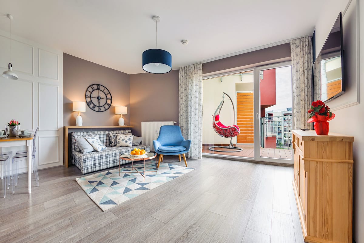 A modern living room with a sofa, a blue armchair, a wooden cabinet, and a dining area with a table and chairs.