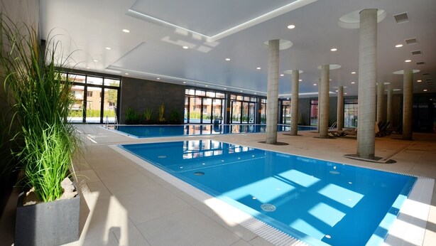 A large indoor swimming pool with clear blue water, surrounded by columns and potted plants. - Apartamenty Sun&Snow Polanki Park (Kolobrzeg)