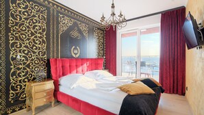 A bedroom with a red upholstered bed, a chandelier, and a large window with red curtains. - Apartamenty Sun&Snow Polanki Park (Kolobrzeg)