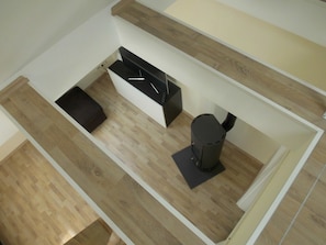 Una habitación moderna y funcional con suelo de madera, un sofá negro, una mesita pequeña y un cubo de basura negro.