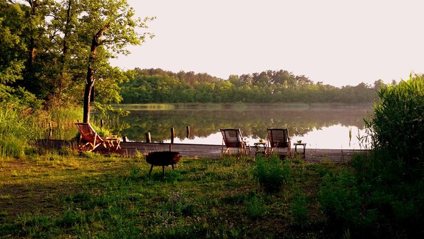 Une terrasse au bord du lac, avec des chaises en bois et un barbecue.