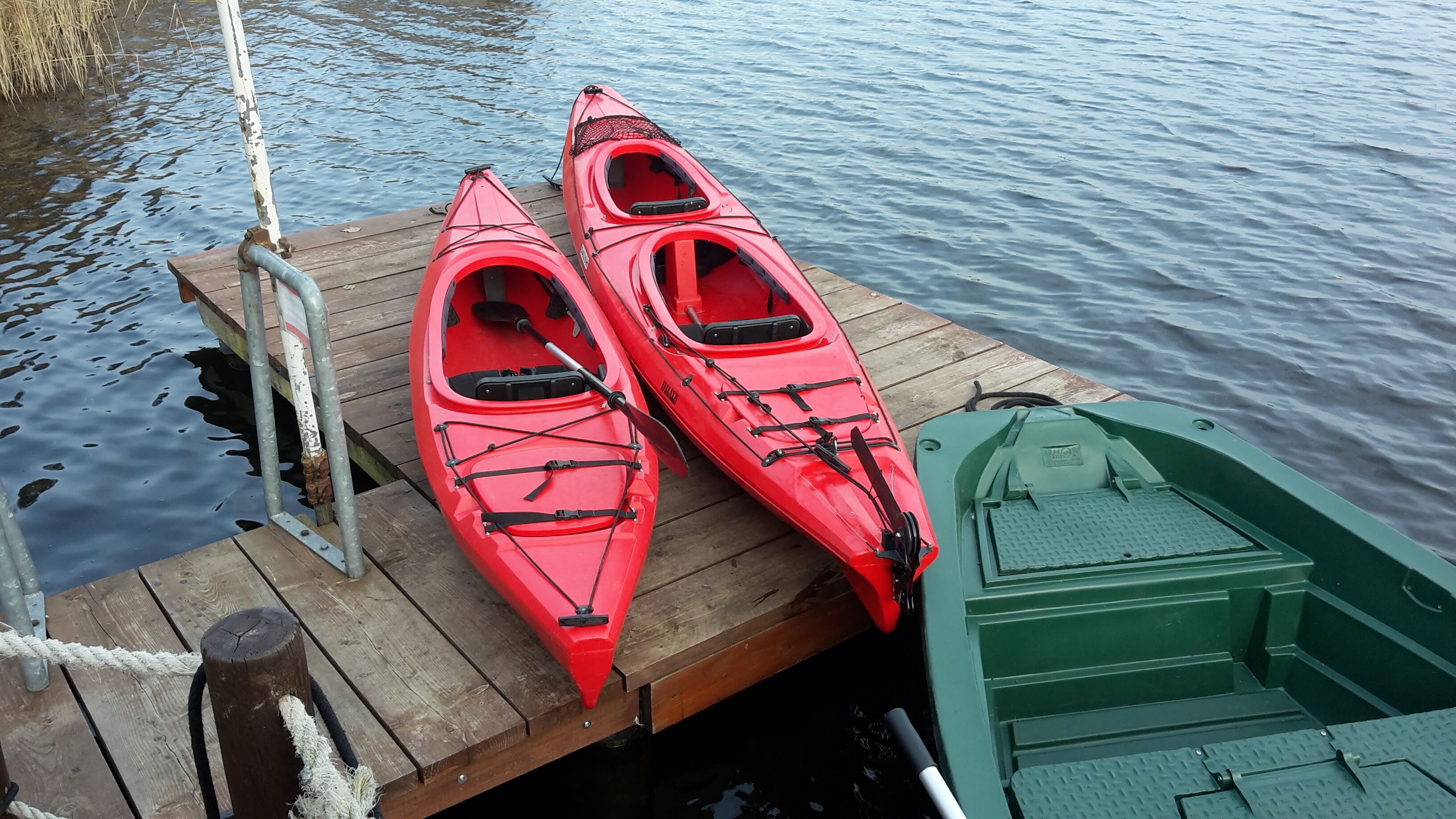 Two red kayaks and a green boat docked at a wooden pier.