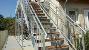 Un escalier menant à un bâtiment dont le toit est recouvert de tuiles rouges, doté de rampes métalliques, et devant lequel est garé un vélo.