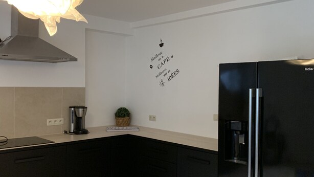 A modern kitchen with black cabinets, a black refrigerator, a coffee maker, and a wall decal. - Petit Coin De Paradis (Charleroi)