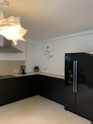 A modern kitchen with black cabinets, a black refrigerator, a coffee maker, and a wall decal. - Petit Coin De Paradis (Charleroi)