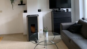 A modern living room with a glass coffee table, a sofa, a fireplace, a TV, and decorative plants. - Petit Coin De Paradis (Charleroi)