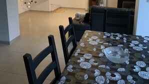 A modern living room with a staircase, a dining area with a patterned tablecloth, and a flat-screen TV mounted on the wall. - Petit Coin De Paradis (Charleroi)