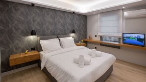 Ein modernes Schlafzimmer mit einem großen Bett, zwei Nachttischen, einem Fernseher und einem Fenster mit Jalousien.