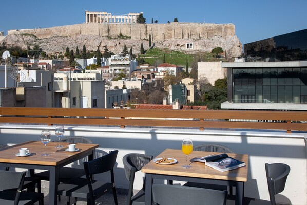 A terrace with tables and chairs, overlooking a historic cityscape with ancient ruins.