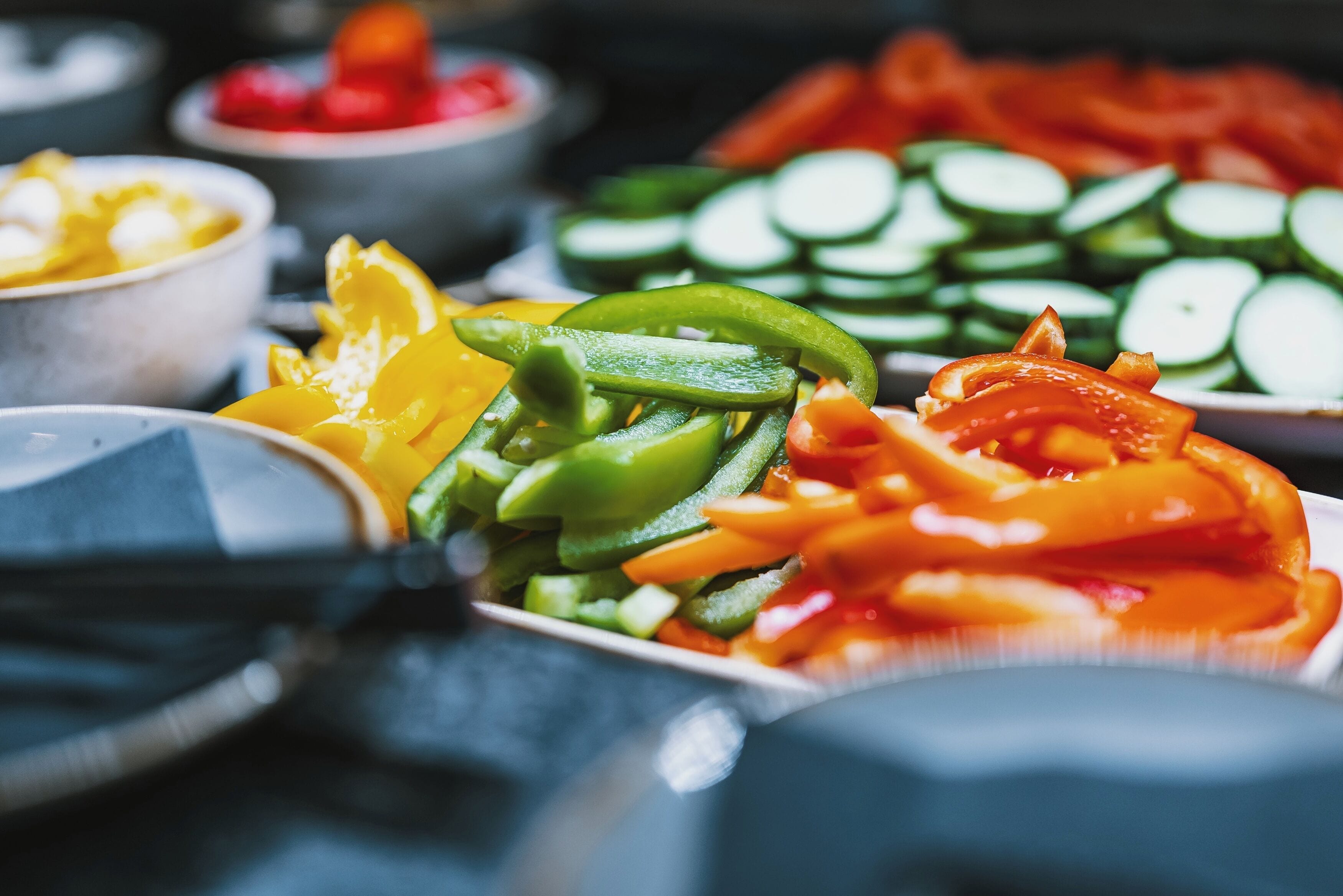 A variety of sliced vegetables including cucumbers, bell peppers, and possibly onions, arranged on a table.