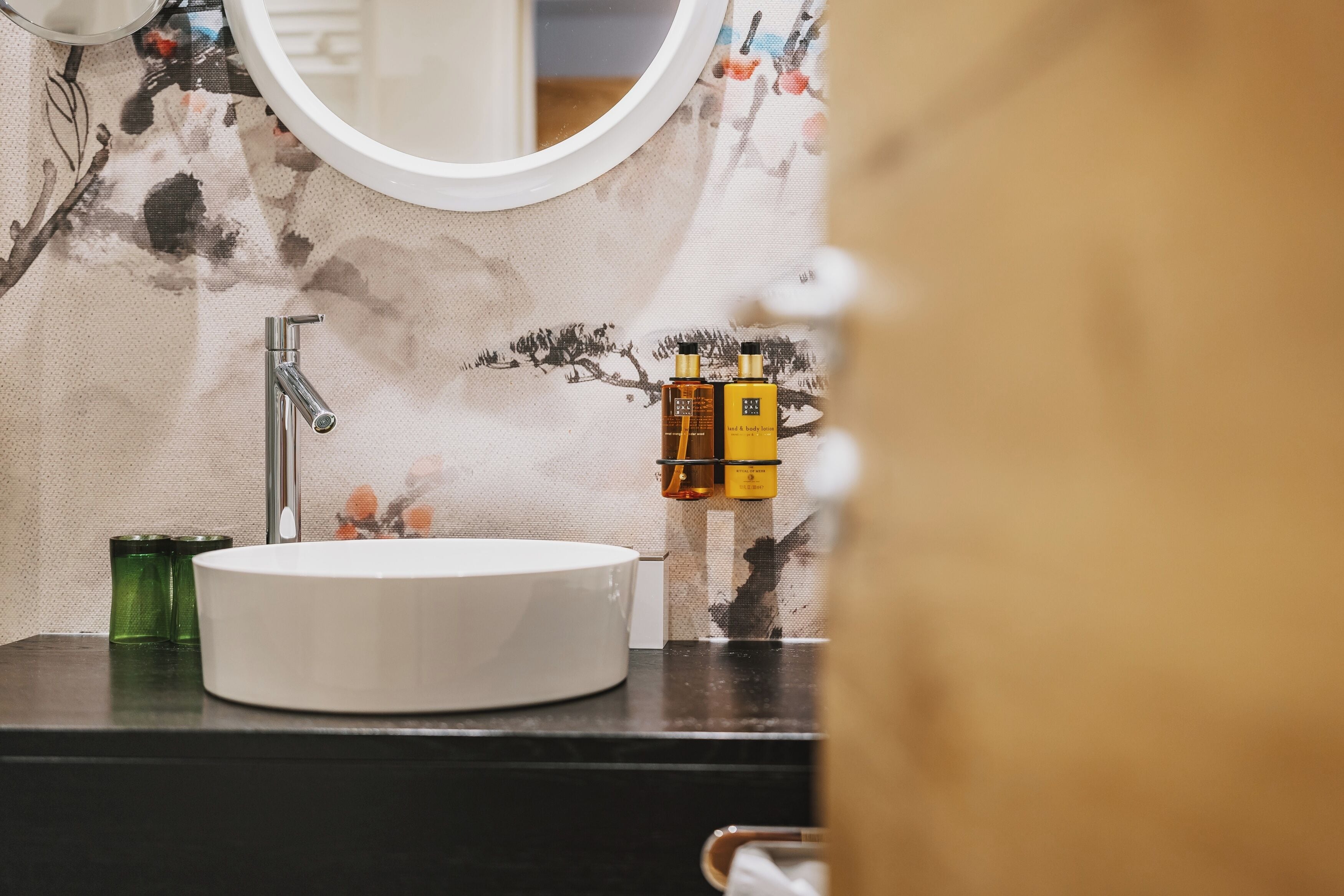 Een badkamer met een rond wit wastafel, een spiegel en twee flesjes lotion op het aanrecht.