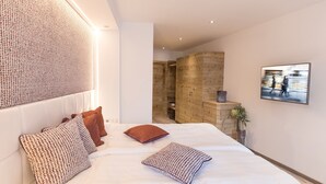 A modern bedroom with a large bed, a stone wall, and a framed picture on the wall. - Hotel Flachauerhof  (Flachau)