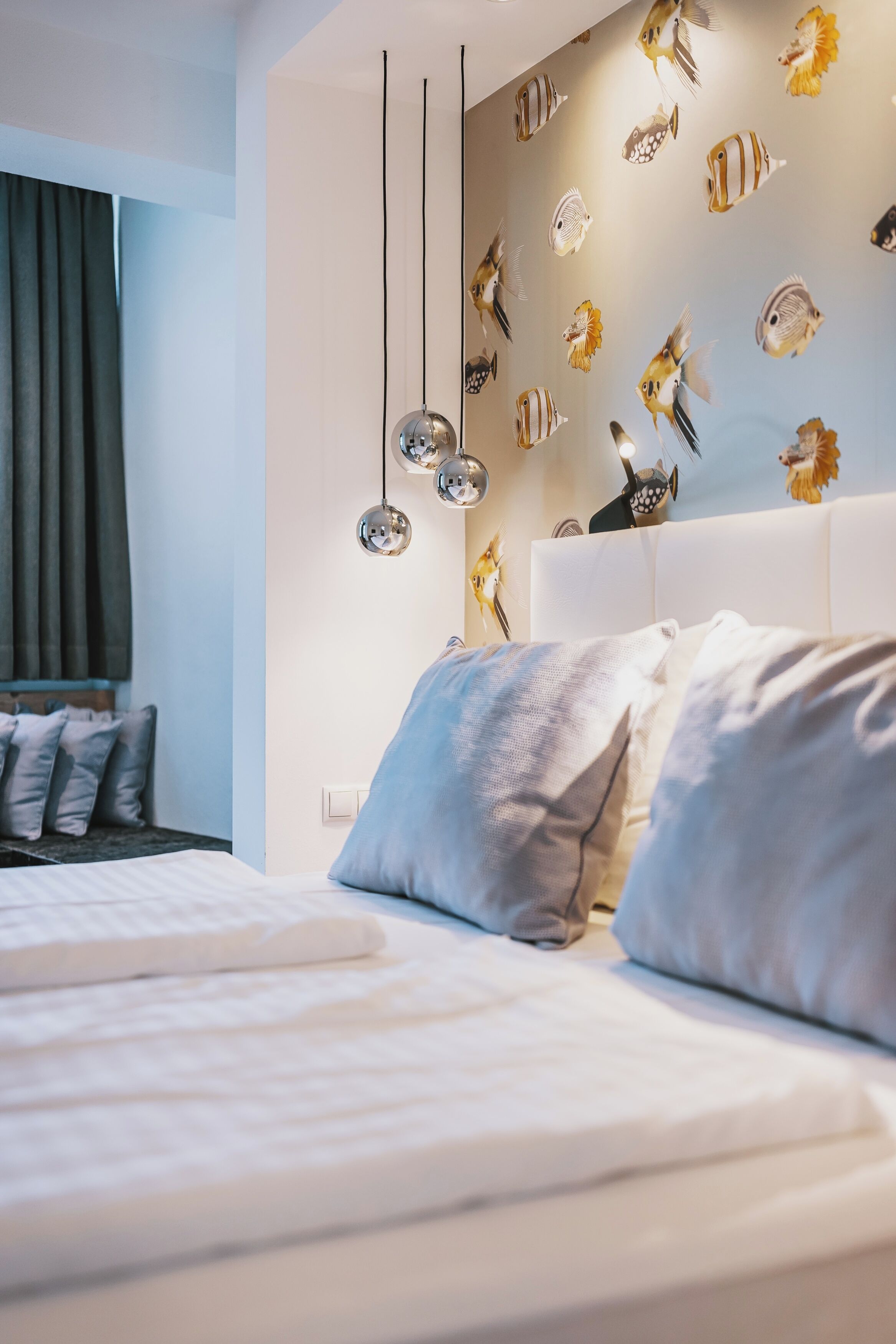 A modern bedroom with a white bed, grey pillows, and a wall decorated with fish decals.