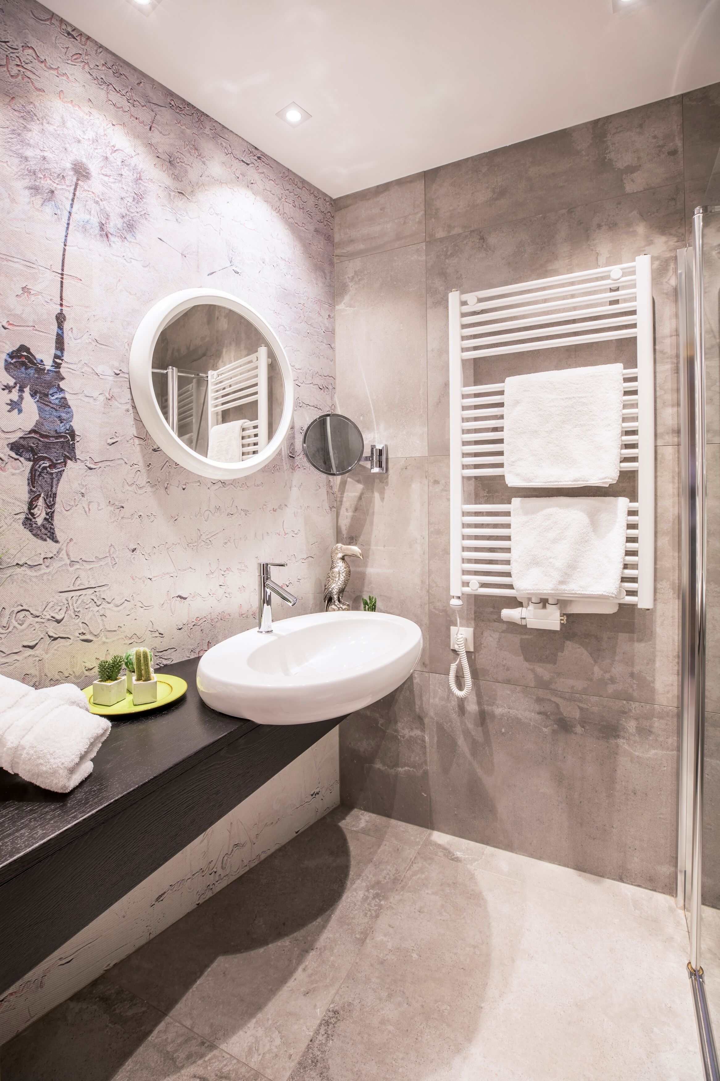 Une salle de bain moderne avec un miroir rond, un lavabo blanc, un porte-serviettes et un espace douche.